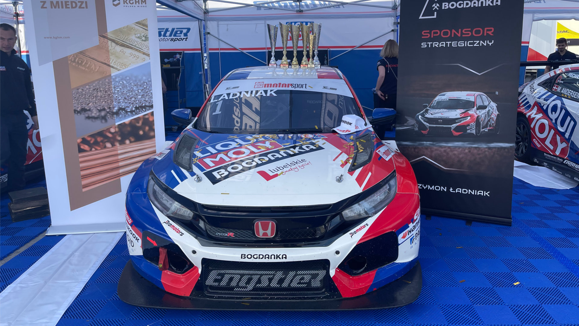 Szymon Ładniak race car with trophies at the team stand